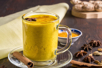 Golden latte milk tea made with turmeric and spices on wooden background. 