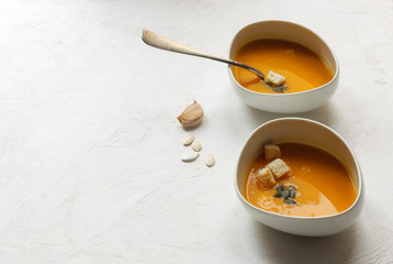 Pumpkin soup with croutons and seeds in white bowls on a white background with space