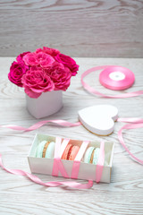 Pink roses in a gift heart shaped box on white wooden table. sweet macaroons  as a present with ribbon, spring background.