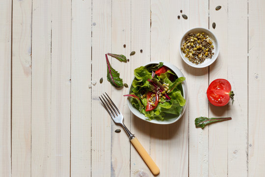 mixed salad with Munga bean sprouts and pumpkin seeds, top view on light boards with space