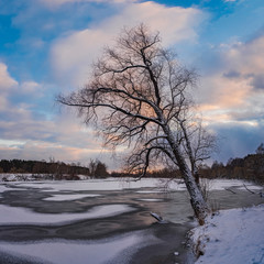 Beautiful winter landscape with frozen river, trees and sunset sky