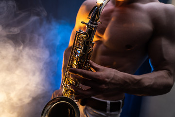 Obraz na płótnie Canvas Muscular man with naked torso playing on saxophone with smoked colorful background 
