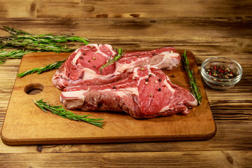 Raw fresh beef rib eye steaks on bone with spices and rosemary on wooden table