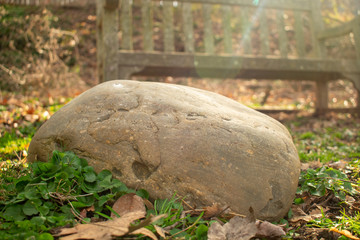 A Large Round Rock With an Old Park Bench Behind it and Sunrays