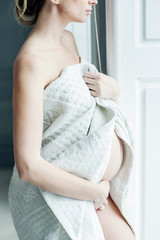 Portrait of a happy pregnant girl European race. She caresses the belly and take cover in a blanket on a light background. Soft focus.