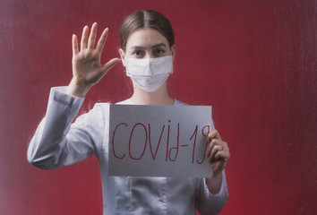 a young doctor stands behind a glass insulator on a red background with a sign in her hands that...