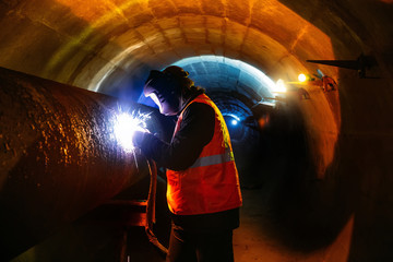 Worker in protective mask welding pipe in tunnel