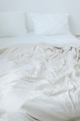 Fototapeta na wymiar Crumpled beige bed linen. Scandinavian style white bedroom 