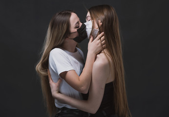 Two young girls hug and kiss in medical masks during the coronavirus pandemic on a dark background