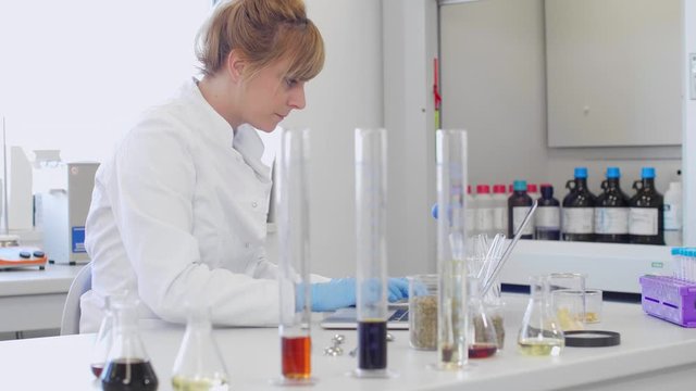 Chemist working with hemp CBD oil in laboratory and writing results in laptop.
