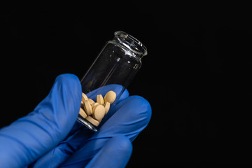 Bottle of flu antiviral pills drug researched, speeds up coronavirus recovery in early trials of COVID-19, blue rubber glove hand. Active against virus SARS-CoV-2. Unproven in ebola disease curation