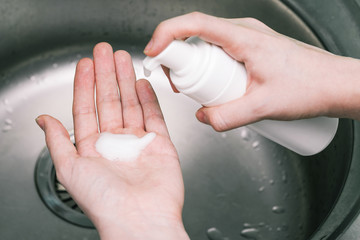 Antibacterial disinfectant in a white plastic bottle. Female hands click on a bottle dispenser. Coronavirus epidemic prevention.