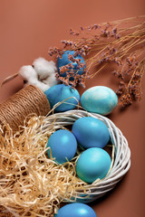 Fototapeta na wymiar Dyed easter eggs in the nest and cotton flowers an a brown background. Easter card with blue decorated eggs in a rustic style.