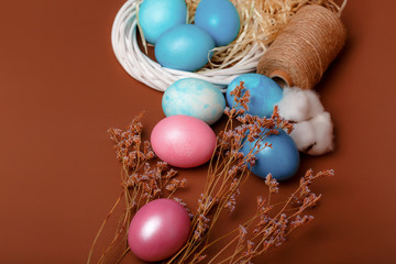 Dyed easter eggs in the nest and cotton flowers an a brown background. Easter card with blue decorated eggs in a rustic style.