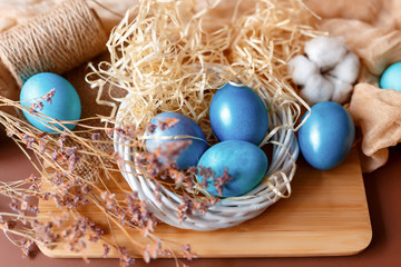 Fototapeta na wymiar Dyed easter eggs in the nest and cotton flowers an a brown background. Easter card with blue decorated eggs in a rustic style.