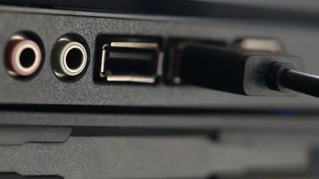 USB cable is inserted into socket. Black panel with colored connectors for microphone and headphones, and also Universal Serial Bus connection ports close-up. Macro of hand inserting black cable