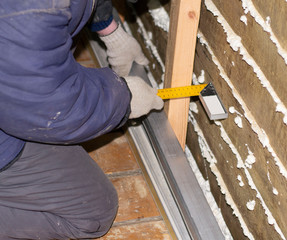 Worker in a blue jacket makes measurements on a piece of wood at a construction site.