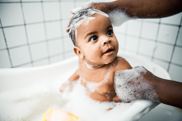 Afro American man washing hair of adorable newborn child