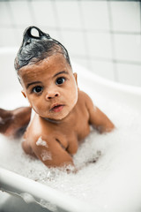 Cute Afro American baby sitting in bathtub with foam