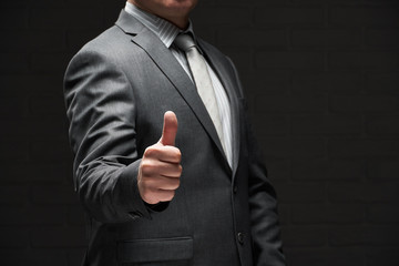 businessman portrait showing best gesture, thumb up, dressed in gray suit, dark wall background
