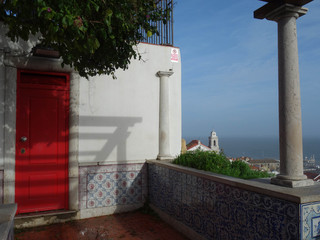 View from above of Lisbon with sitting and meditation porch from the miradouro S.ta Luzia next to a house with a red door.