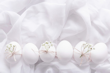 Fototapeta na wymiar White Easter eggs with flowers and green leaves on white textured background