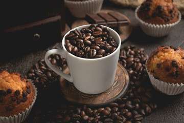 cup of coffee beans surrounded by chocolate muffins, shadows