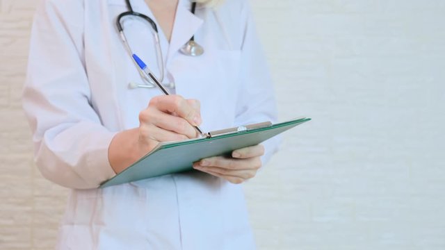 Unrecognizable female woman doctor writing a diagnosis, case medical history on a prescription board