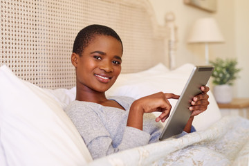 Smiling young woman using a tablet while lying in bed