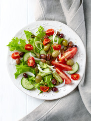 Healthy salad with various tomatoes, cucumber, olives and capers. White wooden background. Top view.