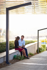 Smiling young businesspeople using a tablet while sitting outside