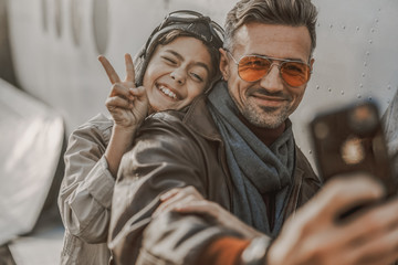 Smiling dad using smartphone and making selfie with his son