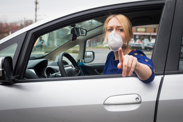 A woman in the driver's seat of her vehicle wears a mask to protect against the coronavirus