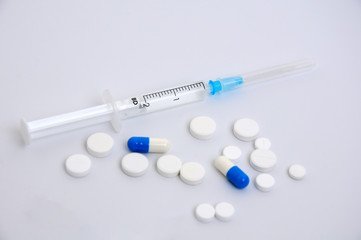 heap of medical tablets and syringe on a white background