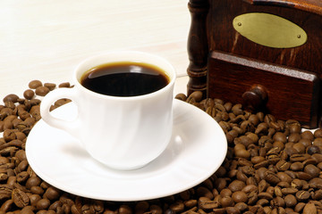 A white cup of coffee and coffee beans on a wooden table.