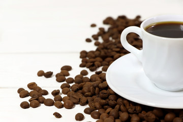 A white cup of coffee and coffee beans on a wooden table.