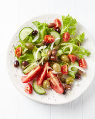  Healthy salad with various tomatoes, cucumber, olives and capers. White wooden background. Top view.