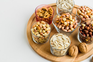 Shelled nuts varieties with walnuts,hazelnuts,pistachio,almonds and seeds in glass bowls on wooden tray,half view