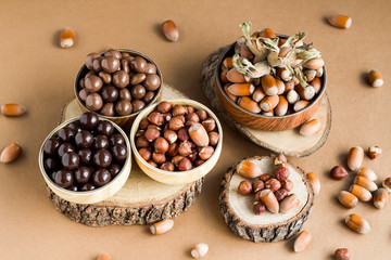 Milky and dark chocolate covered hazelnuts in bamboo bowls on wooden table with natural hazelnuts.