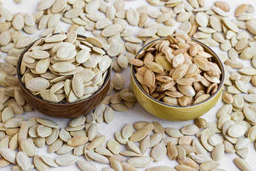 Two different types  pumpkin seeds in the bamboo bowls at the white surface with many seeds.