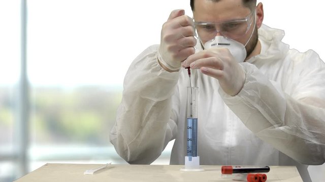 Smart scientist experimenting in a lab to invent medicine. Stirring reagent with blood test. Man's researching and developing.