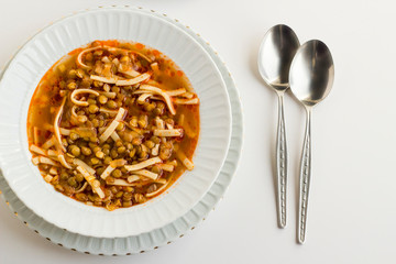 Traditional Turkish,green lentil soup cooked with tomato paste and noodles on the white background with spoon.