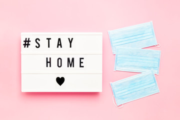 Three medical protective masks and STAY HOME written in light box on pink background. Healthcare...