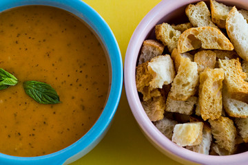 Traditional Turkish red lentil soup and crusty bread in the mini cookware,on the yellow background.Taken from above.Half view of soup and bread.