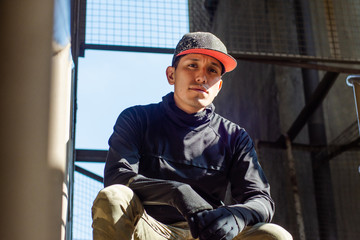 Handsome young man sitting at urban place wearing a cap