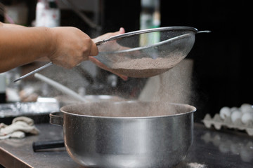 female cook hands sifting cocoa for the preparation of a sweet cake