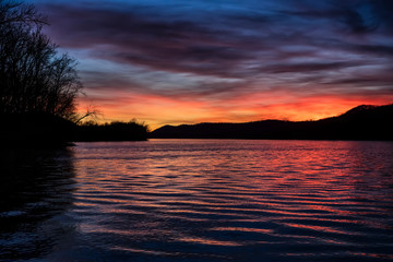 Fototapeta na wymiar The sunset paints the sky over the hills of the Ohio River Valley with beautiful color as reflections dance on the surface water ripples. Ohio is viewed from the West Virginia river bank.