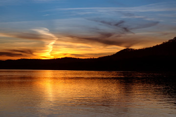 The sunset paints the sky over the hills of the Ohio River Valley with the reflection of fading evening light upon the calm water as photographed from the West Virginia shore.