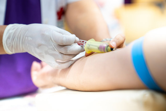 Medical person drawing blood with syringe and hypodermic needle from a patient.