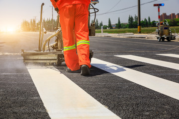 Road workers use hot-melt scribing machines to painting pedestrian crosswalk on asphalt road...